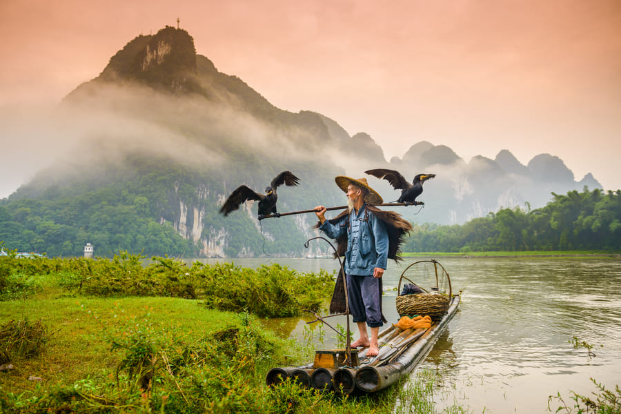hombre parado en una canoa con unas montañas de yangshuo de fondo